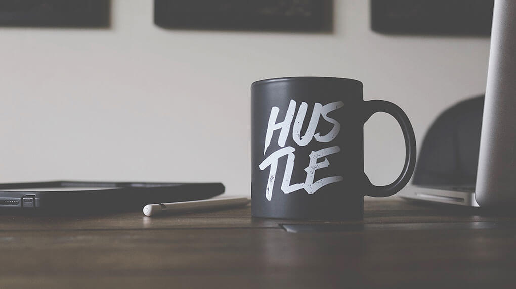 black mug with  text Hustle on the desk