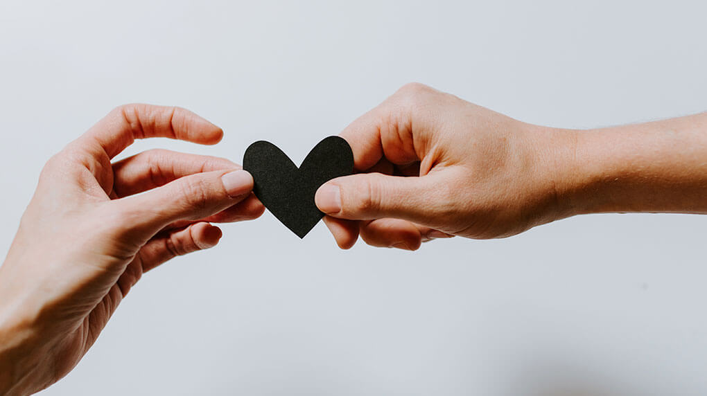 two people sharing a small black paper heart